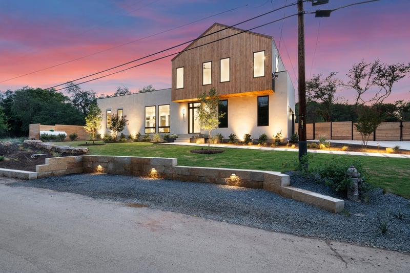 Wide-angle front corner view of custom home illuminated by landscape lighting in Austin, TX by J. Angelo Design Build