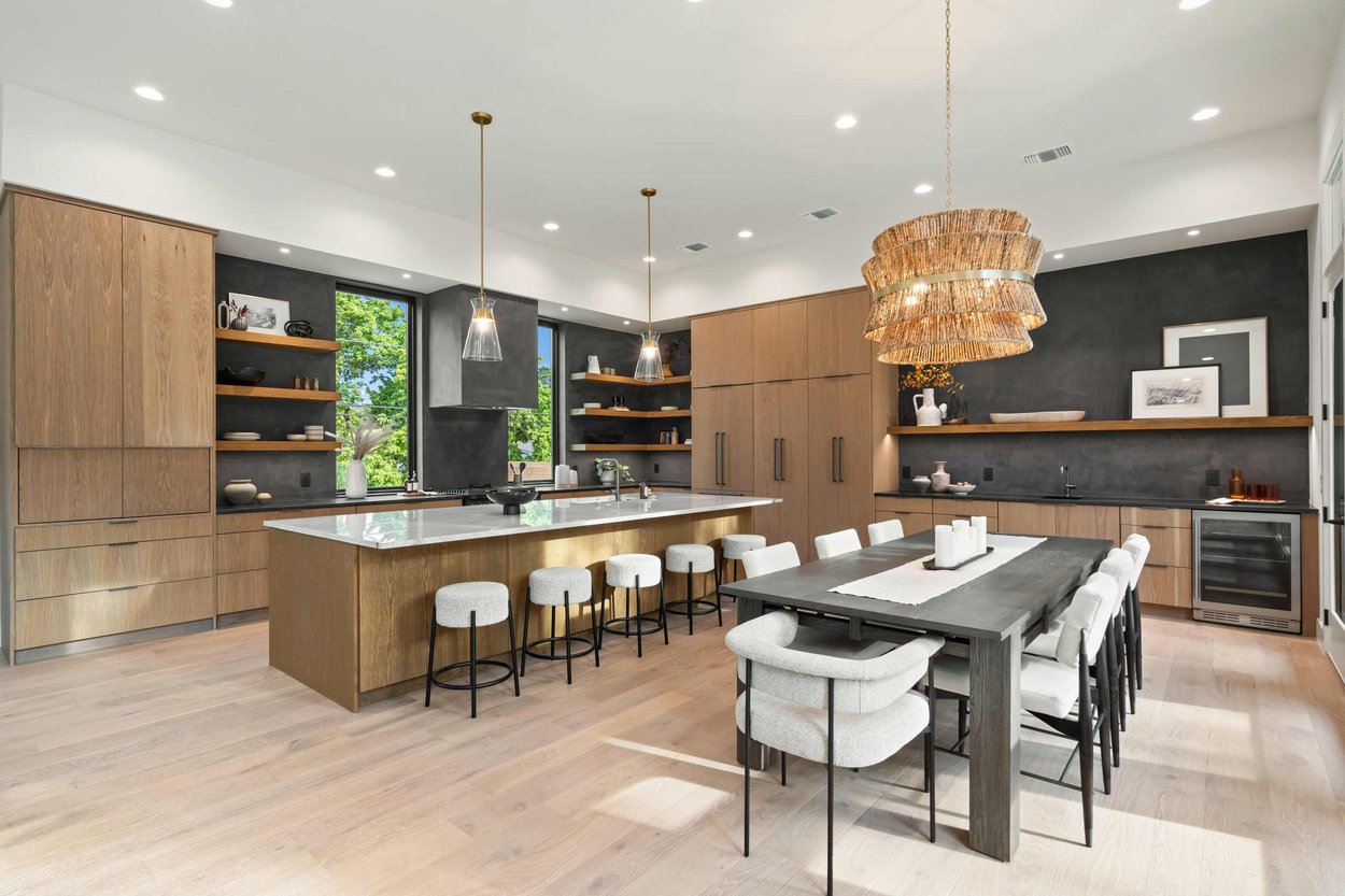 Modern open-concept kitchen and dining area in a custom home by J. Angelo Design Build in Austin, TX featuring light wood cabinetry, a large central island, black and white countertops, and open shelving. Modern open-concept kitchen and dining area in a custom home by J. Angelo Design Build in Austin, TX featuring light wood cabinetry, a large central island, black and white countertops, and open shelving.