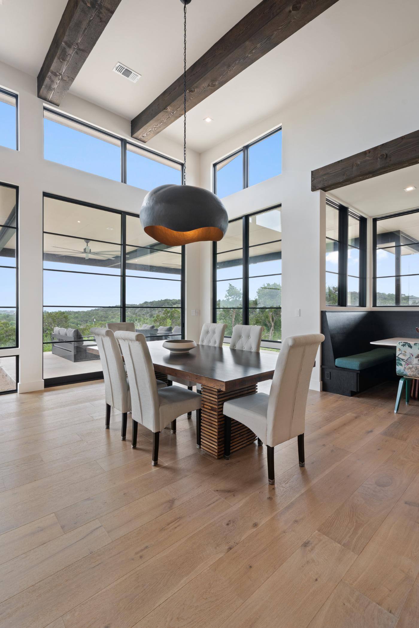 Dining table area in open floor plan featuring large windows and chandelier in custom home built in Austin, TX by J. Angelo Design Build