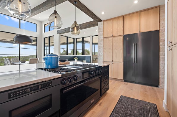 View from behind kitchen island gas stovetop, oven, microwave, and storage drawers in custom home by J. Angelo Design Build in Southwest Austin, TX