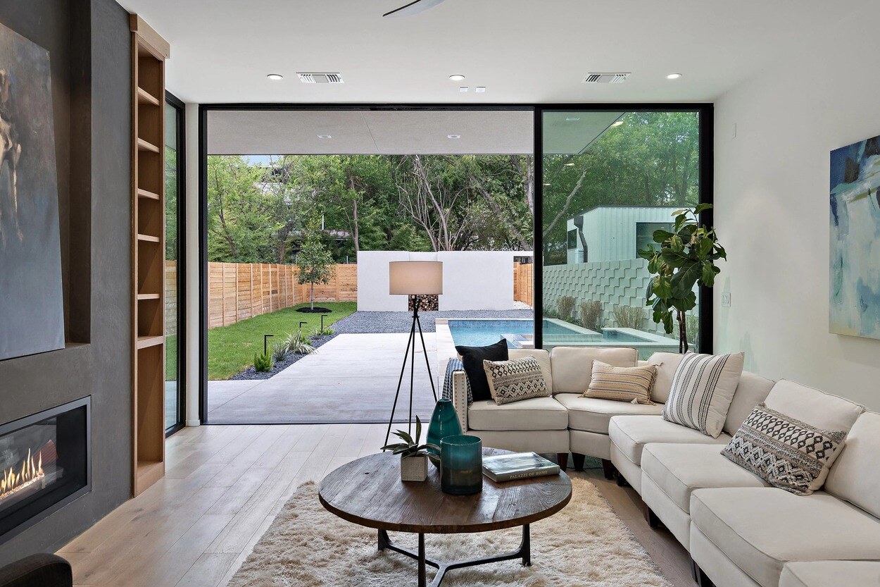 Luxurious living room with floor-to-ceiling glass doors leading to a modern backyard with a pool in a custom home in Austin, TX by J. Angelo Design Build