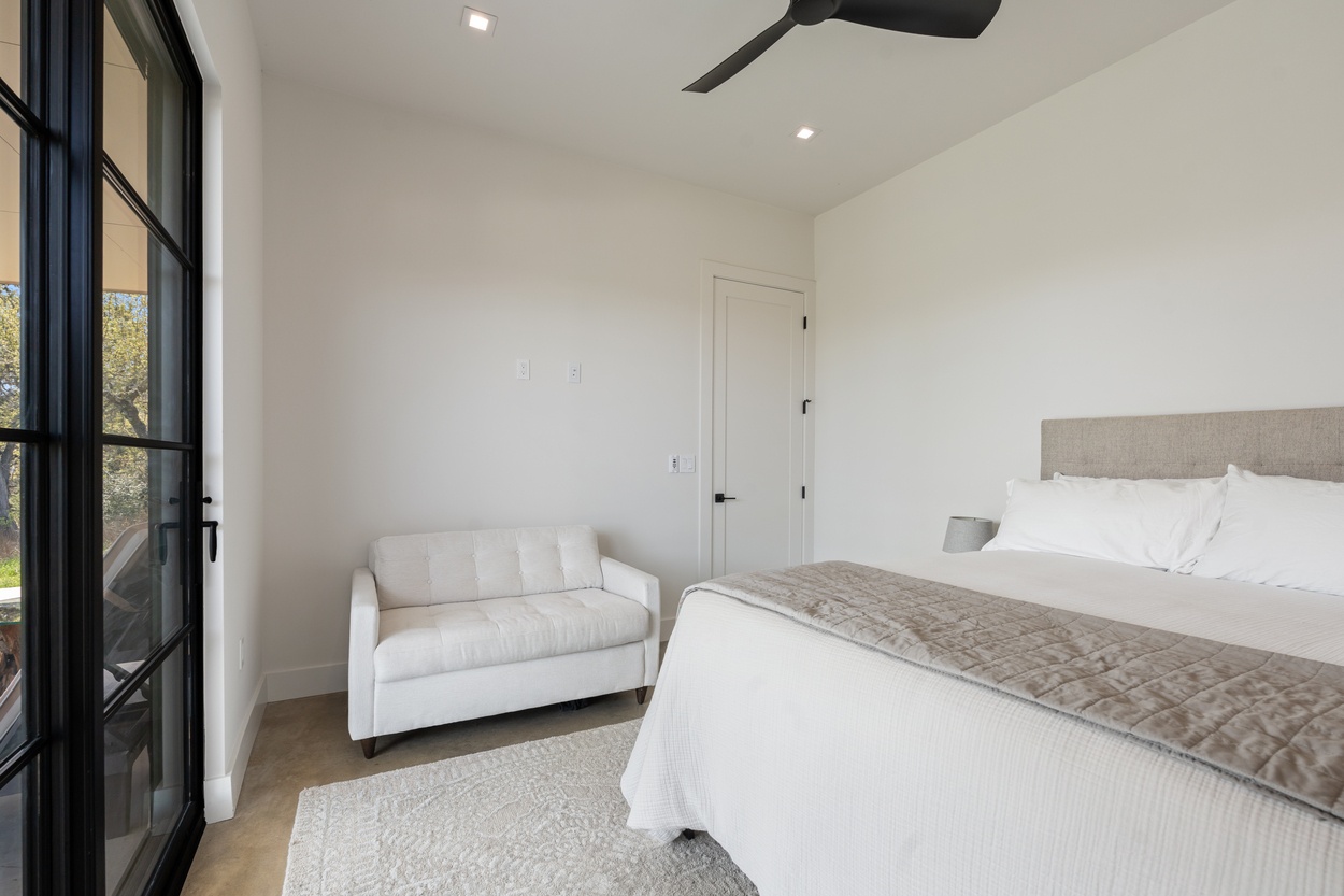 Minimalist bedroom with white loveseat and glass patio door in a detached casita by J. Angelo Design Build in Austin, TX