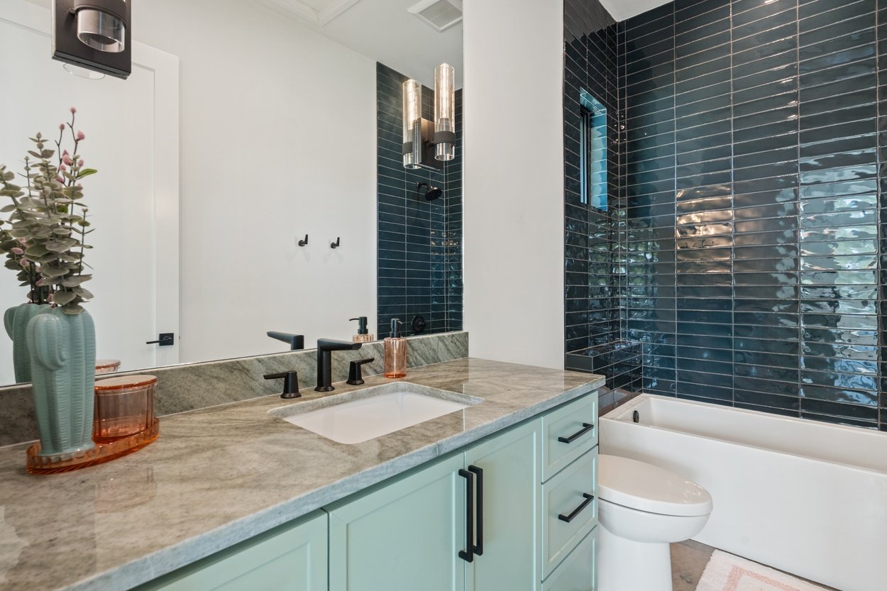 Modern bathroom with glossy dark tile and dual black fixtures in a detached casita by J. Angelo Design Build in Austin, TX