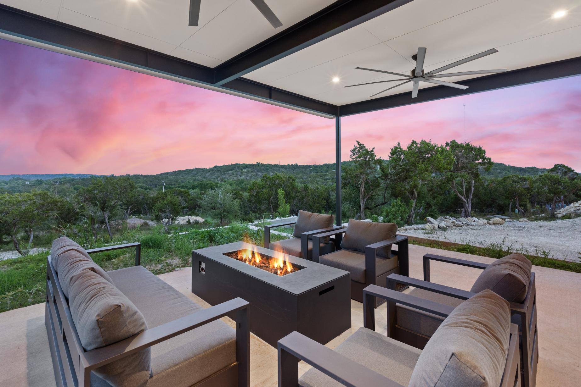 Covered outdoor patio with comfortable seating and a fire pit overlooking a scenic sunset by J. Angelo Design Build