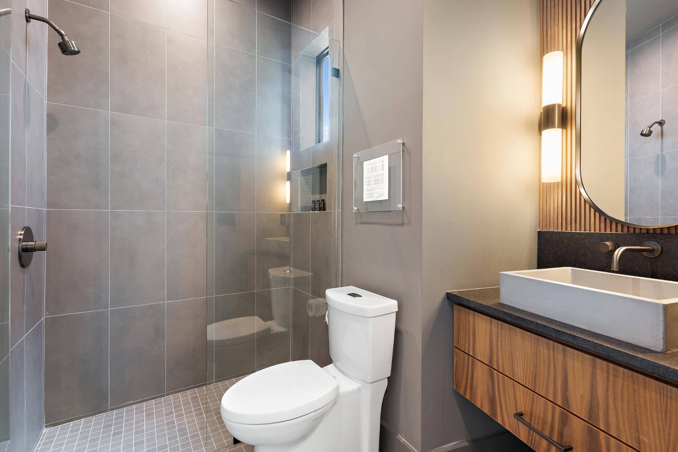 Custom homes bathroom featuring a glass-enclosed shower and grey tile walls by J. Angelo Design Build in Southwest Austin, TX