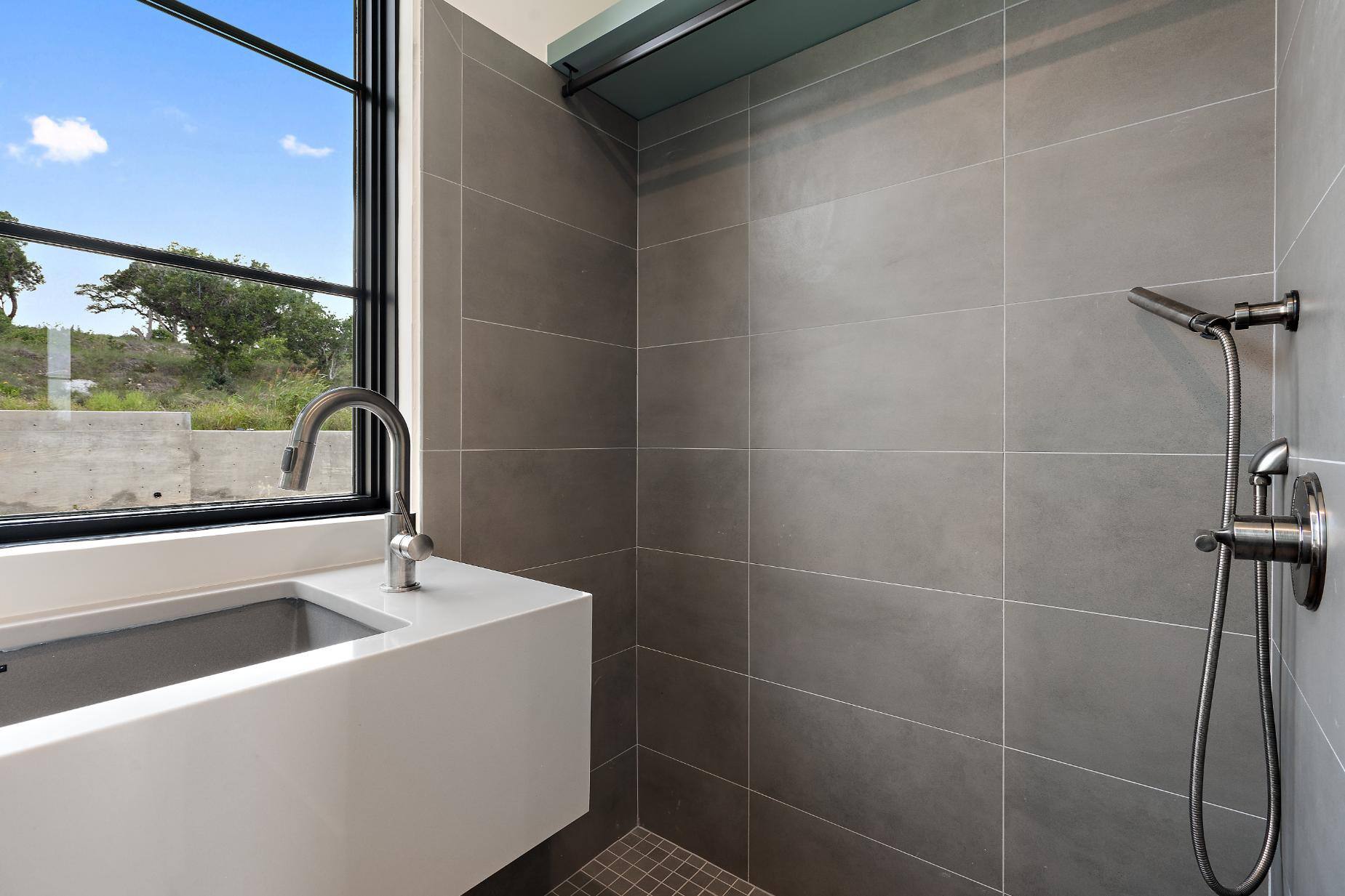 Custom homes sleek shower space with large windows and grey tile design by J. Angelo Design Build in Southwest Austin, TX