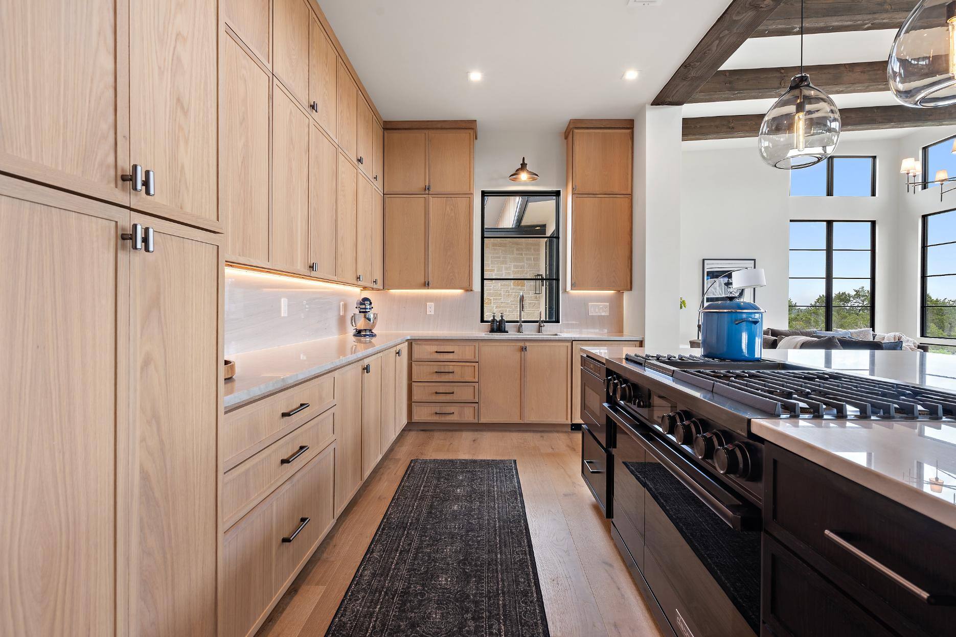 Kitchen area from from fridge featuring cabinetry, sink area, and kitchen island with stove in custom home built in Austin, TX by J. Angelo Design Build