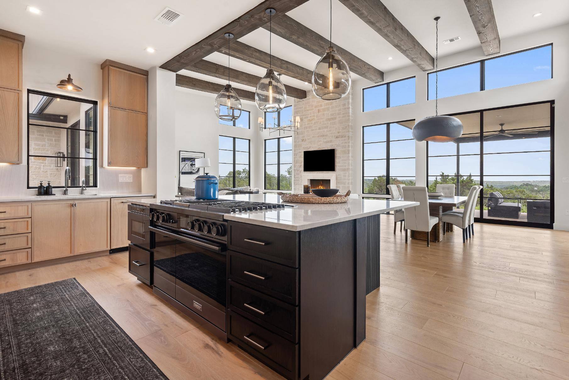 Kitchen island view of open floor plan featuring gas stove, oven, microwave, storage drawers, larger windows, and exposed beams in custom home by J. Angelo Design Build in Southwest Austin, TX