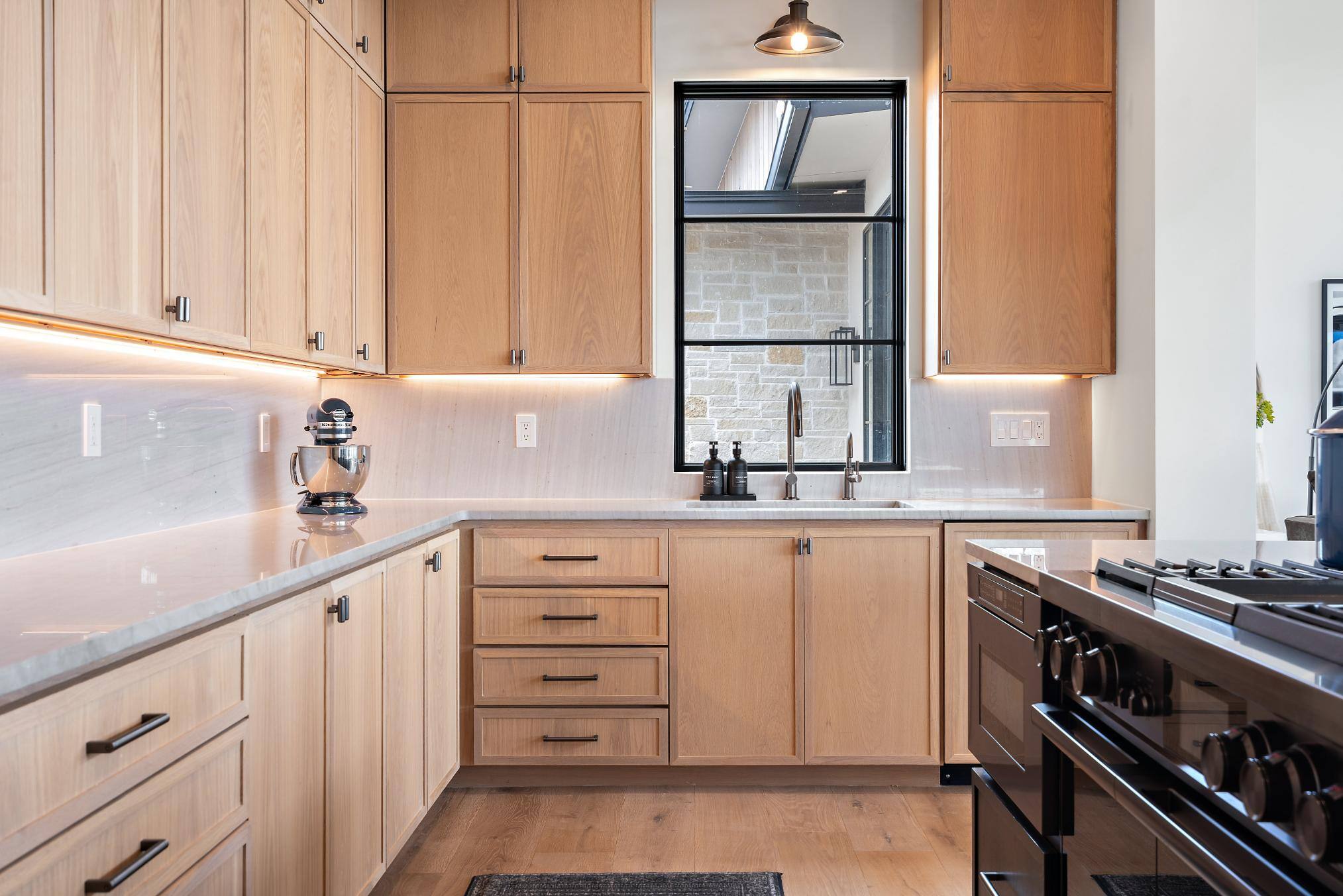 Kitchen sink area featuring above-the-sink window, light wood cabinetry, and gas stove in custom home built in Austin, TX by J. Angelo Design Build