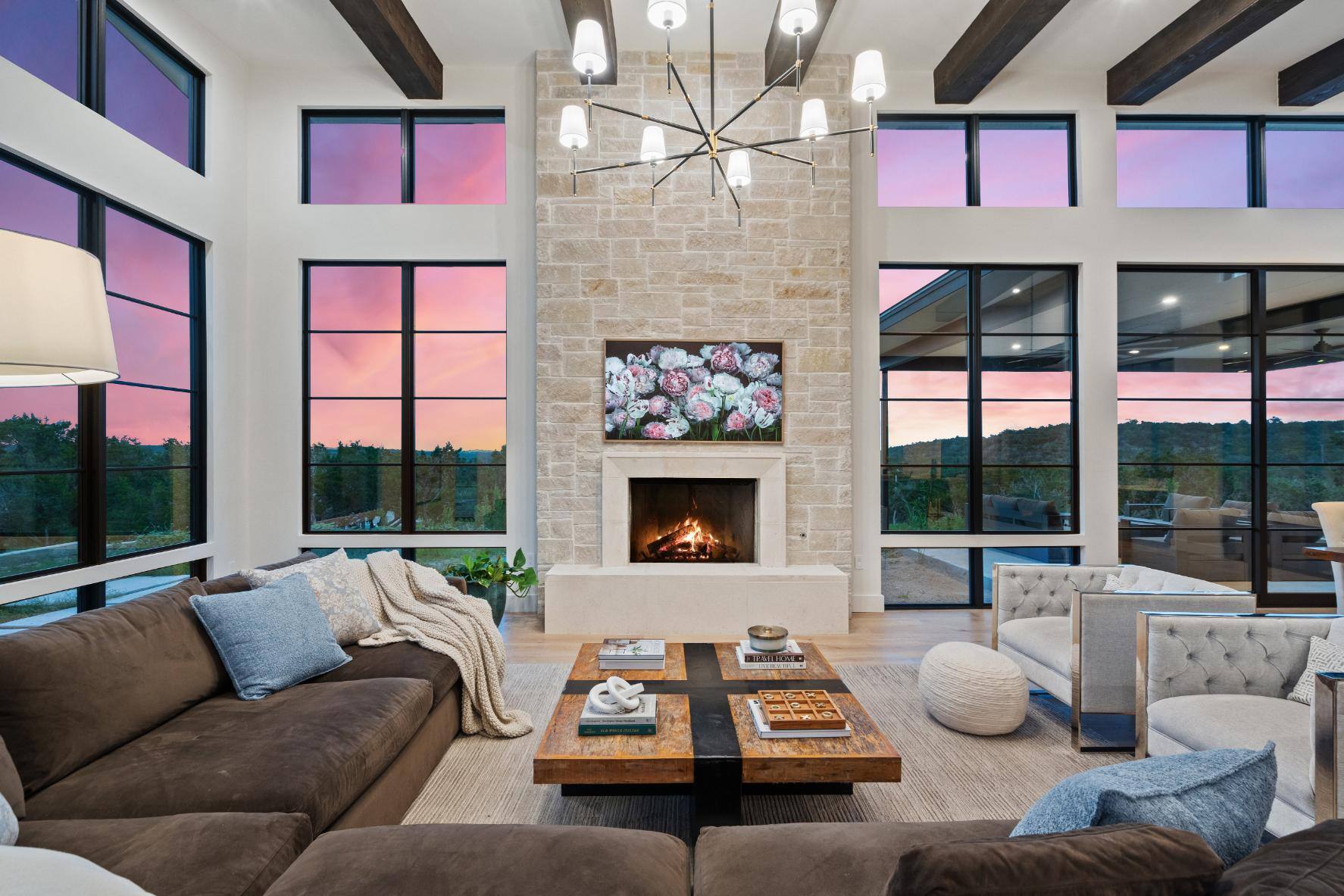 Modern living room with a stone fireplace and large windows overlooking a sunset by J. Angelo Design Build