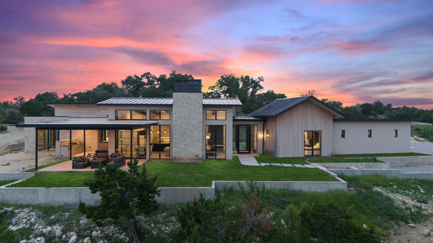 Sunset view of a modern custom home by J. Angelo Design Build in Southwest Austin, TX, featuring a central chimney and large glass windows