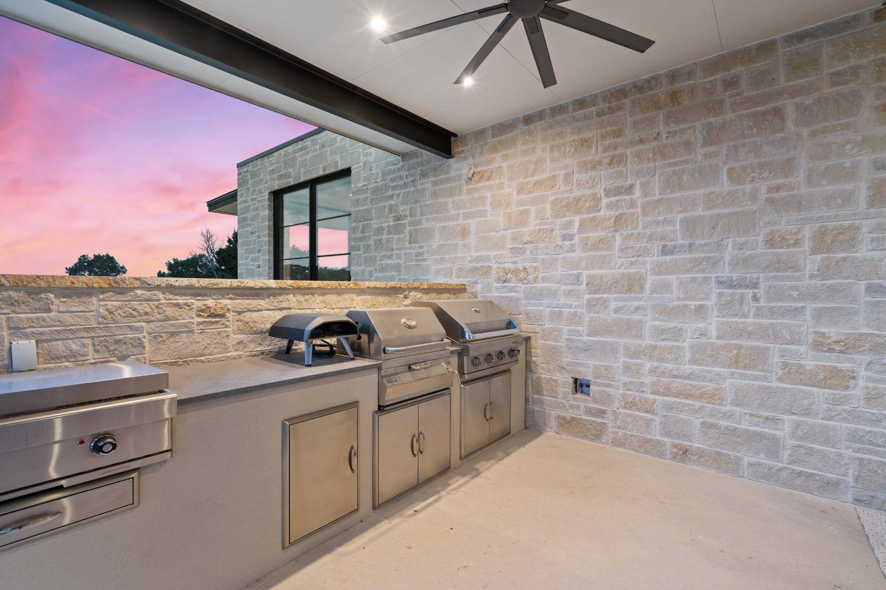 Outdoor kitchen area featuring stainless steel grill and stone backsplash and wall by J. Angelo Design Build