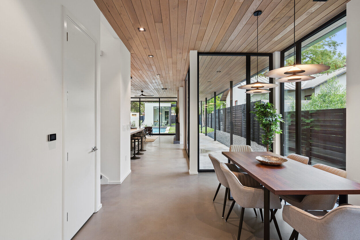 Open-concept dining space featuring contemporary lighting and a view of the outdoor pool in a custom home in Austin, TX by J. Angelo Design Build