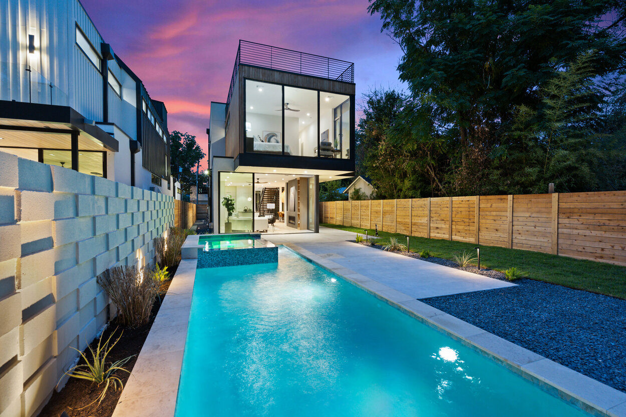 Back exterior and yard of custom home in Austin, TX at dusk featuring pool and patio area by J. Angelo Design Build