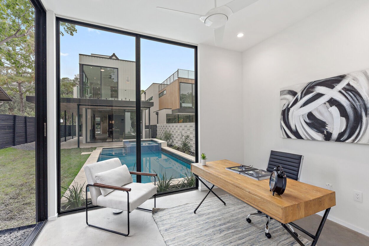 Custom office space with floor to ceiling windows and access to backyard pool by J. Angelo Design Build in Austin, TX